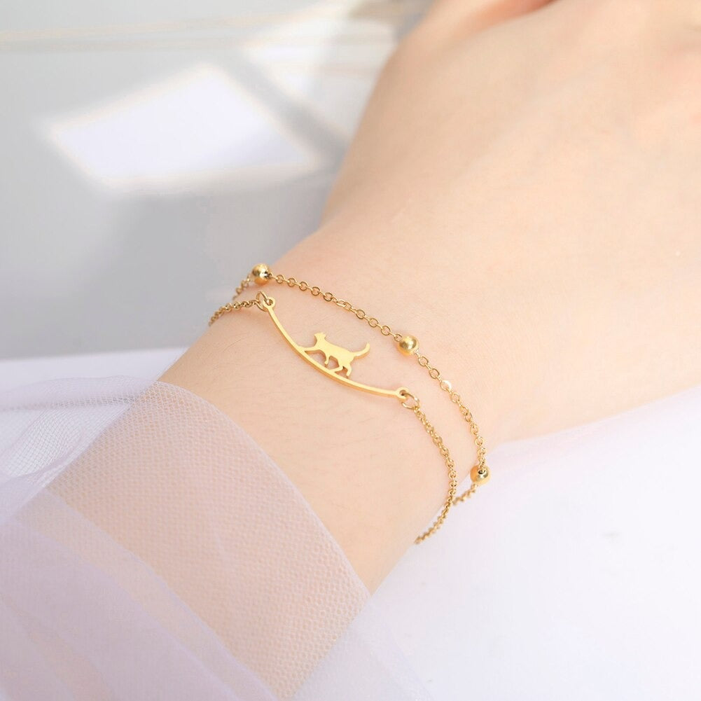 Vrouw draagt goudkleurige dubbele armband met wandelende kat op een randje.